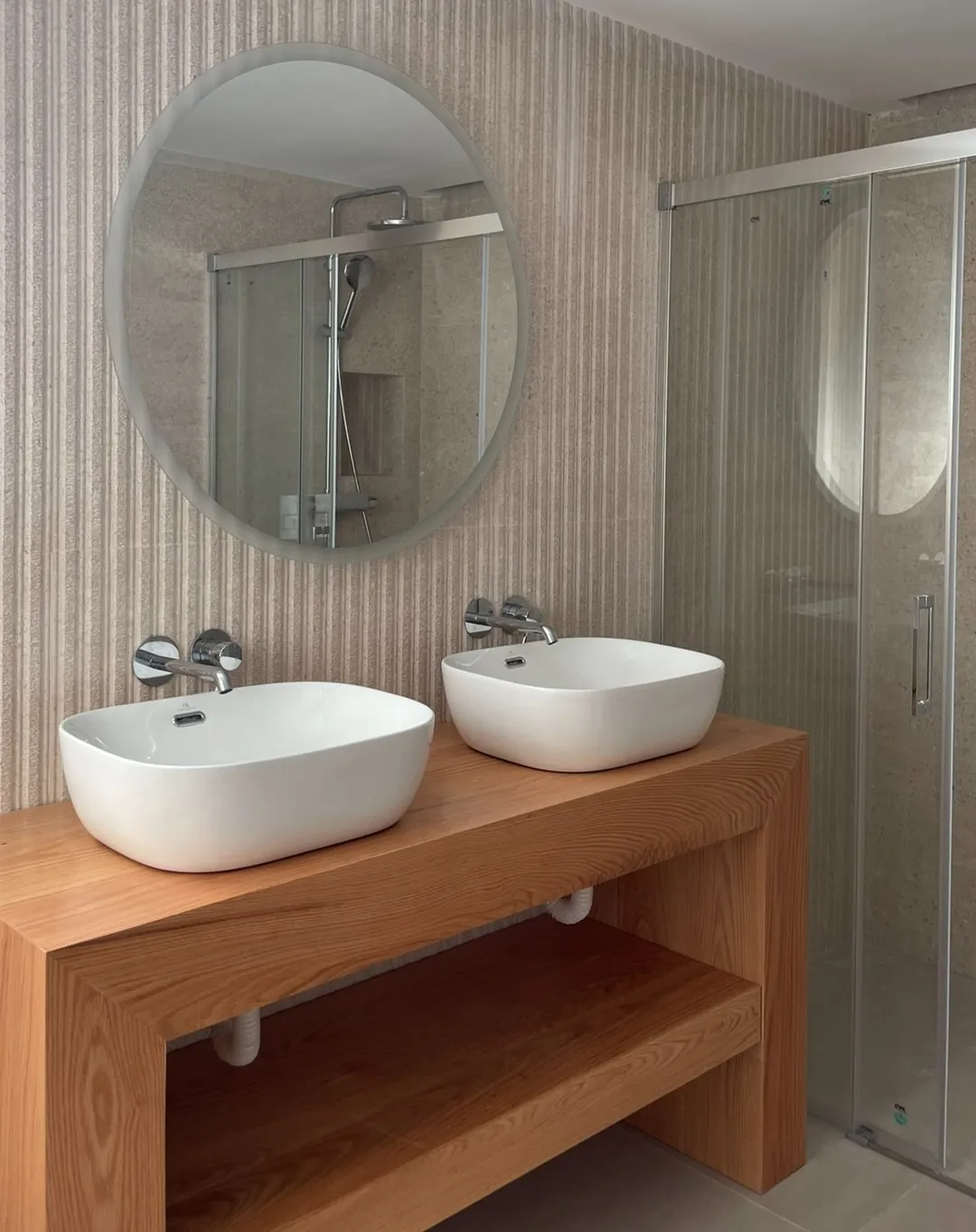 Baño con mueble a medida de madera maciza, dos lavabos y espejo redondo
