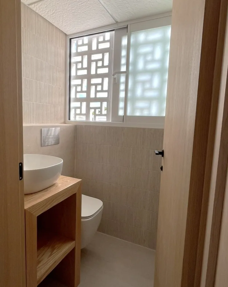 Baño de planta baja con lavabo sobre mueble de madera y celosía en la ventana