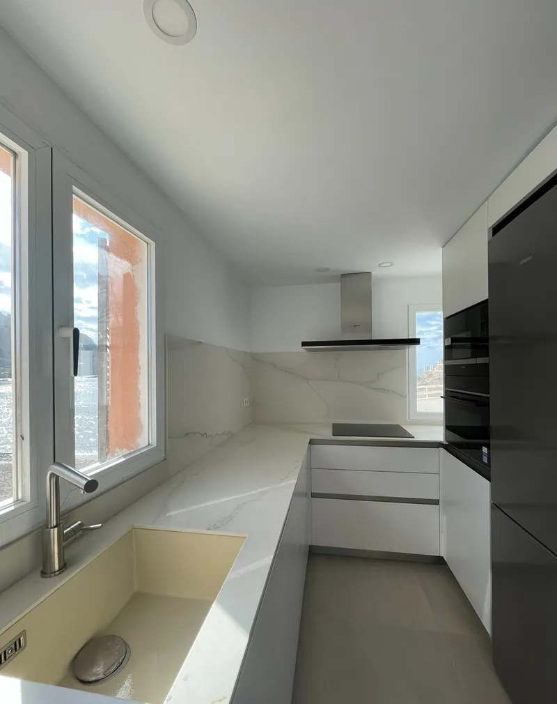Cocina blanca en línea con encimera clara y ventana
