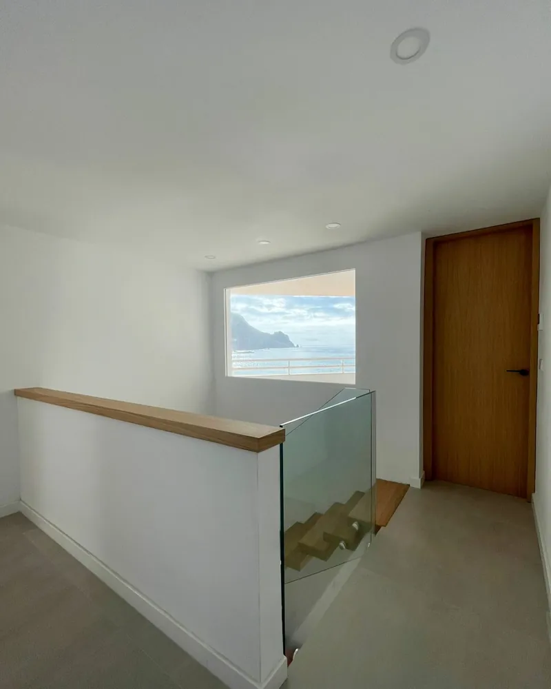 Distribuidor de la planta superior con barandilla de vidrio y ventana al mar