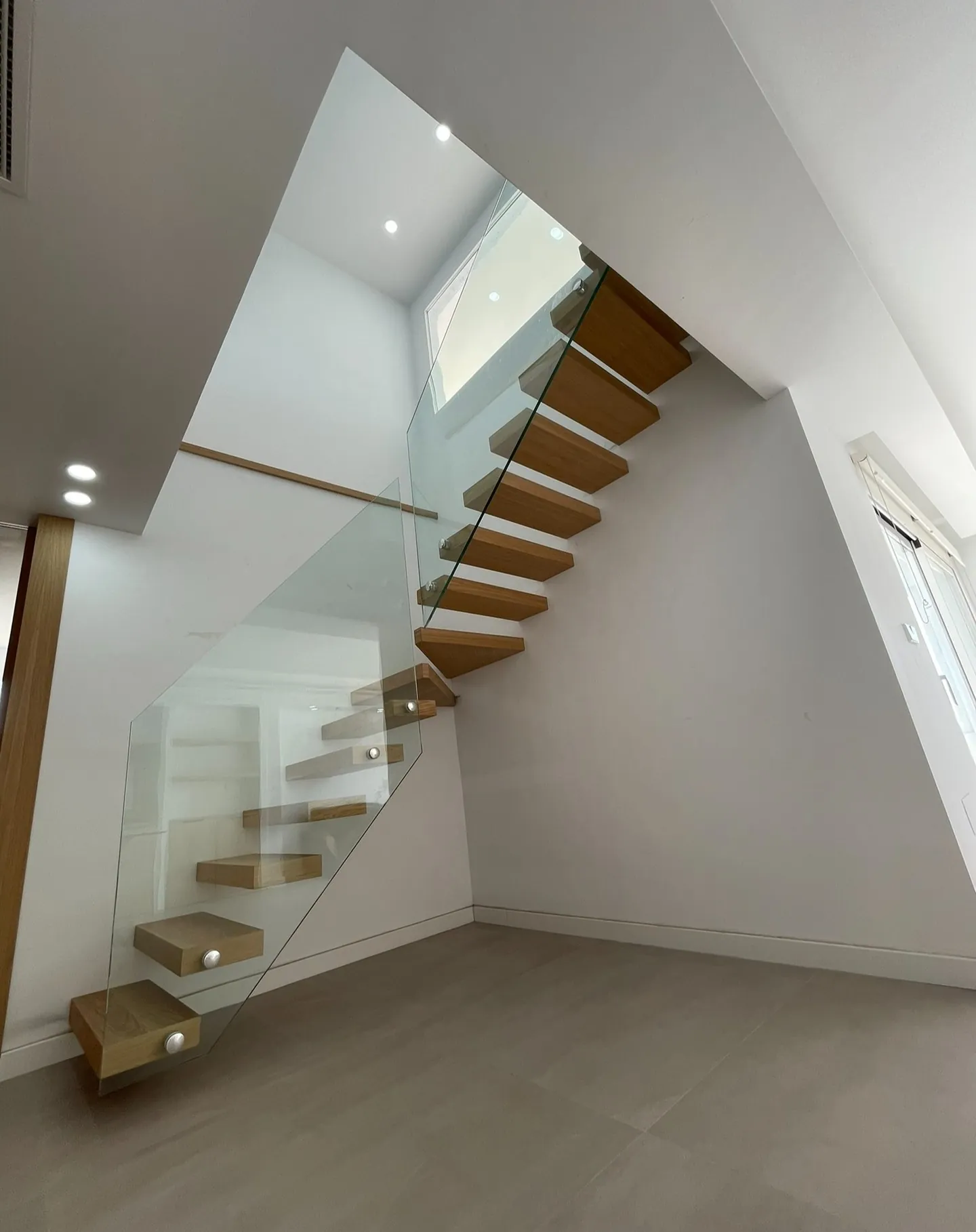 Escalera volada de madera maciza bajo un lucernario, tras la reforma integral