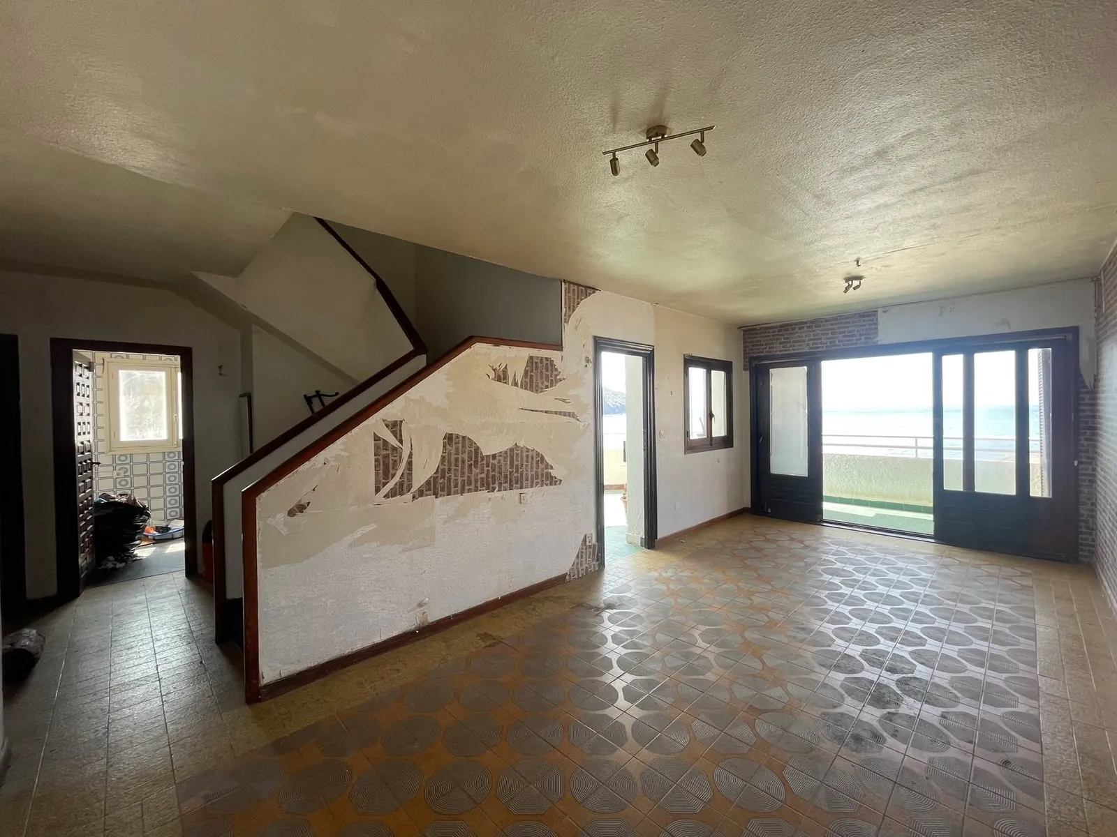 Antes: salón con suelo de baldosa hidráulica, paredes oscuras y escalera de obra